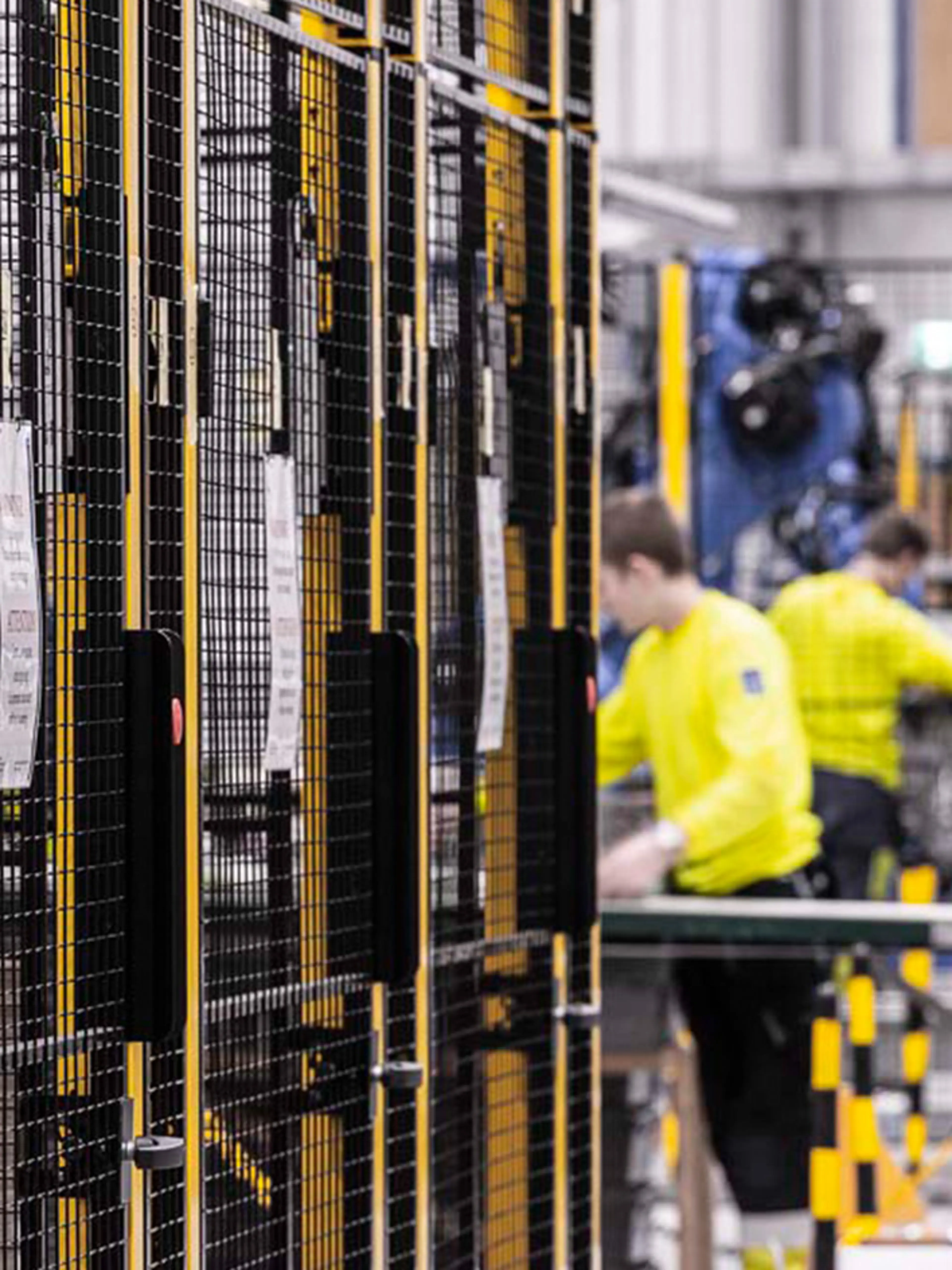 Magazijn met veiligheidsbarrières en werknemers in de buurt van machines, waarbij de risico's worden benadrukt wanneer mensen en automatisering met elkaar interageren.