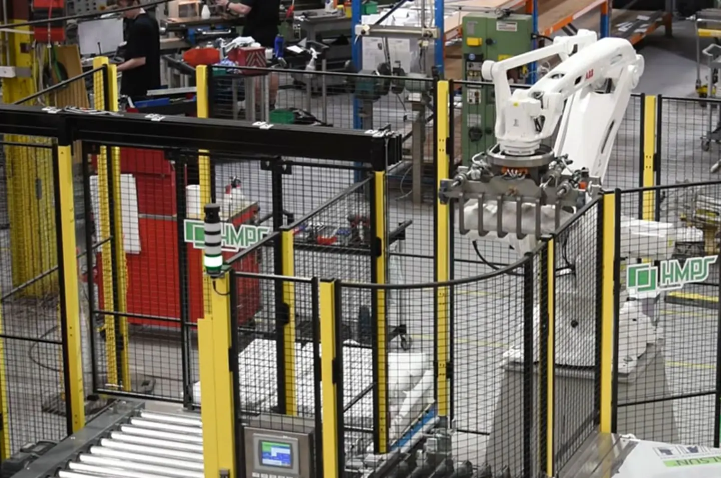 Geautomatiseerde industriële robotarm die werkt in een fabriek met transportbanden en veiligheidshekken