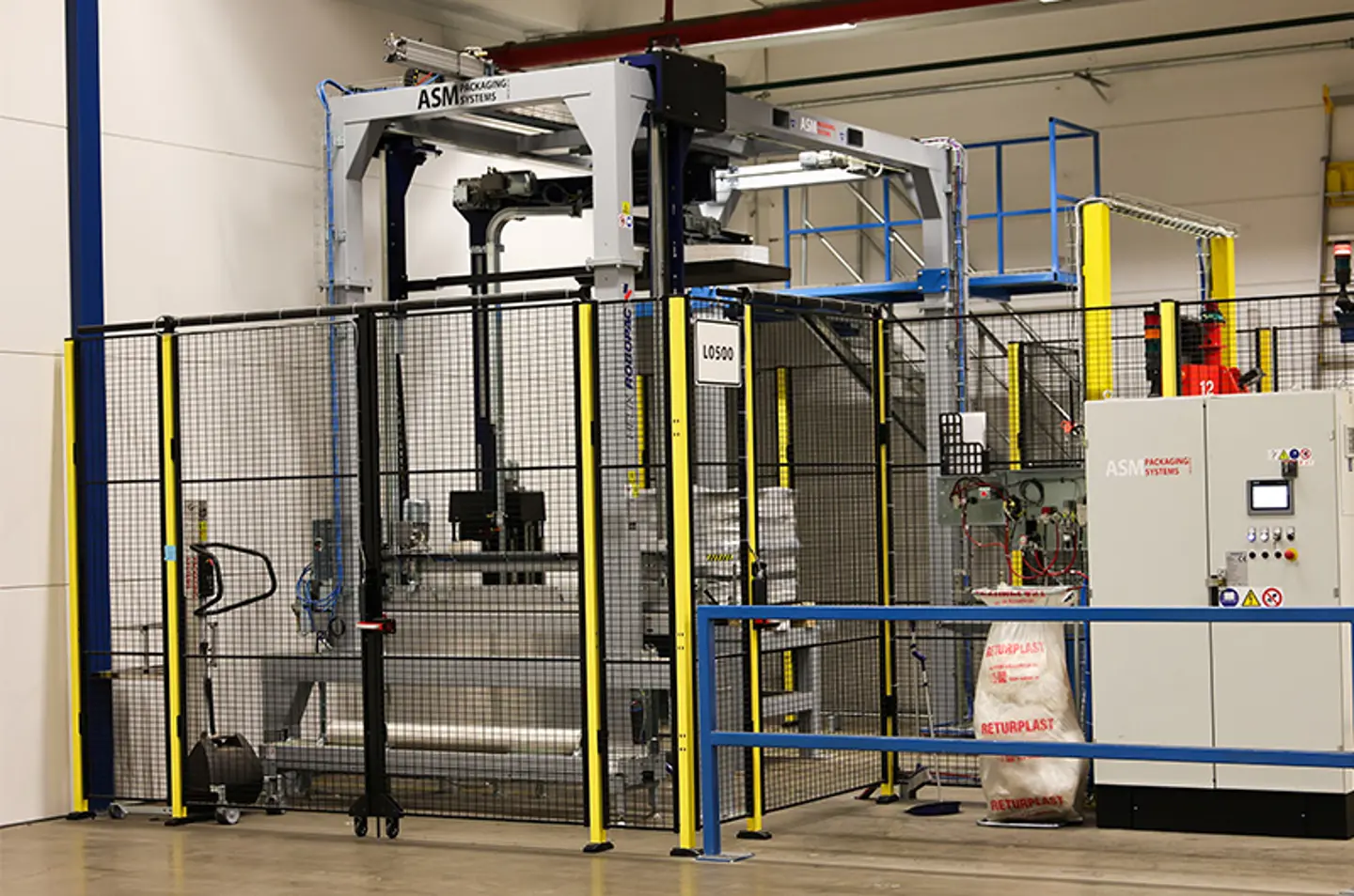 Geautomatiseerd verpakkingssysteem in een magazijn, omgeven door veiligheidshekken en uitgerust met bedieningspanelen